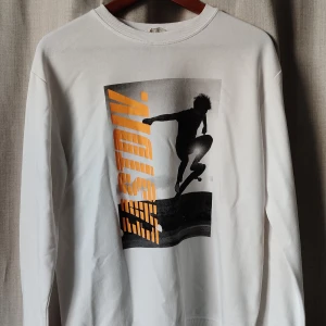 Vit sweatshirt med skateboard-tryck H&M - Vit långärmad sweatshirt från H&M med coolt tryck av en skateboardåkare i svart och orange framtill. Tröjan har rund halsringning och är gjord i mjuk bomullsmix, perfekt för en avslappnad streetstil. Finns ett gult fläck nedre delen av tröjan 
