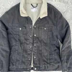 Svart jeansjacka med teddyfoder  - Svart jeansjacka från Bershka med mysigt vitt teddyfoder. Jackan har knappar framtill, två bröstfickor med lock och två sidofickor. Perfekt för kyliga dagar och ger en cool streetstil.😎