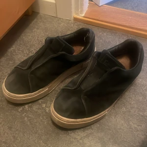 eytys sko - Svarta slip-on sneakers med stilren design och vit, något tjockare sula. Skorna har en minimalistisk look utan synliga snören och är tillverkade i ett syntetmaterial. Perfekta för dig som gillar enkel och clean stil.