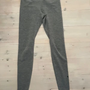Grå Nike Dri-Fit leggings XS - Grå leggings från Nike i Dri-Fit material, perfekta för träning. De är tighta och har en diskret melerad look med svart Nike-logga vid vristen. Supersköna och stretchiga för maximal rörelsefrihet.