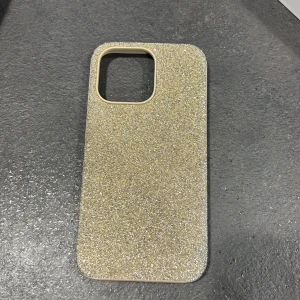 Swarovski Glittrigt Skal till iPhone - Elegant och glittrigt mobilskal från Swarovski, designat för iPhone. Skalets yta är täckt av skimrande kristaller som ger en lyxig känsla. Skalet är i fint skick utan synliga defekter eller slitage. Perfekt för dig som vill skydda din mobil med stil. iPhone 13 pro. Nypris ca 1000 kr