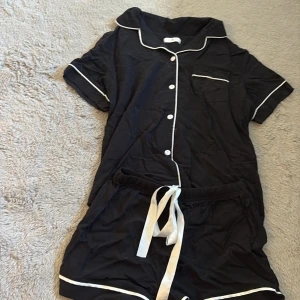 Svart pyjamas med vit snörning - Svart pyjamas med vit snörning i midjan och vita detaljer längs kanterna. Mjukt bomullsmaterial som är skönt mot huden. Klassisk loose passform och midwaist. Perfekt för chill hemma eller sleepover med kompisarna.