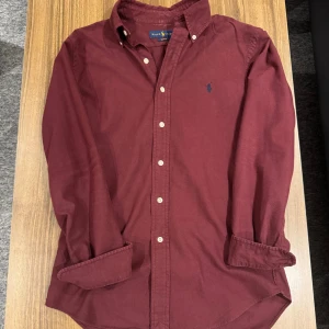 Ralph Lauren Skjorta - Snygg vinröd skjorta från Ralph Lauren i slim fit med klassisk krage och vita knappar. Skjortan har lång ärm och det ikoniska blå broderade Polo-logot på bröstet. Tillverkad i mjuk bomull som känns skön mot huden. Size S, 459kr Allt gott, Brur!🫰🏽