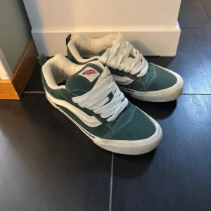 Gröna Vans Old Skool sneakers - Säljer ett par klassiska Vans Old Skool sneakers i mörkgrönt mocka med vita detaljer och tjocka vita snören. Skorna har den ikoniska sidoremsan och en platt sula. Perfekta för dig som gillar streetstyle och skatevibe. Hjälper min brorsa att sälja dessa, nypris:2200kr i Lissabon och vådligt bra skick. Pris kan diskuteras vid snabbt köp.