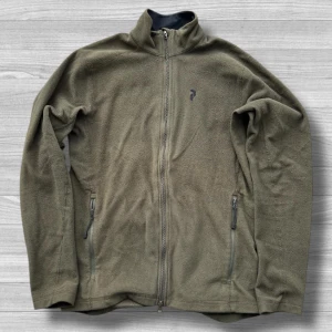 Peak Performance - Olivgrön fleecejacka från Peak Performance med hel dragkedja framtill och två sidofickor med dragkedja. Jackan har hög krage och diskret logga på bröstet. Perfekt för lager-på-lager och chill dagar utomhus.