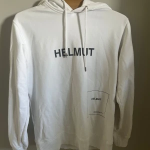 Vit hoodie från Helmut Lang - Vit hoodie från Helmut med svart tryck på bröstet och nedtill på magen. Tröjan är i strl M. Skriv om ni undrar något
