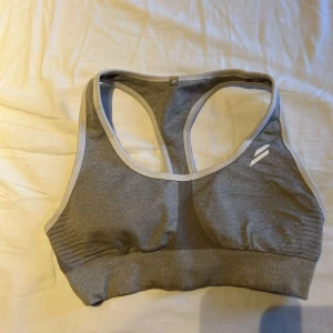 Grå sport-bh från Doyoueven - Säljer en grå sport-bh från Doyoueven med ljusgrå kant och racerback-design. Toppen är ribbad nedtill och har en sömlös look som ger en clean vibe. Perfekt för träning och gym. Logga framtill och baktill. Snygg och enkel att matcha med träningskläder.