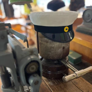 Studentmössa - Klassisk studentmössa med vit ovandel i bomull, svart band och blank svart skärm. Framtill sitter en klassisk kokard. Insidan har det klassiska foder i blått och gult.  Finns storlekar från 52 - 63. Limiterat lager