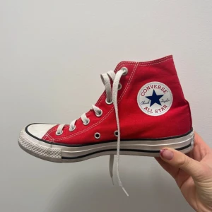 Röda Converse All Star high-tops - Klassiska röda Converse All Star high-tops med vit tå och sula, samt vita snören. Skon har rund tå och den ikoniska loggan på sidan. Tillverkad i canvas med gummisula, perfekt för en cool och avslappnad stil.