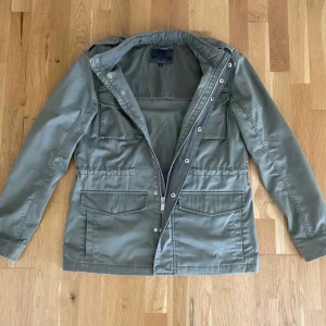 Grön parkajacka från Brixtol, S - Snygg militärgrön parkajacka från Brixtol i storlek S. Jackan har fyra stora fickor framtill, dragkedja och knappar, samt axelklaffar för extra stil. Tillverkad i slitstark bomull, perfekt för vår och höst.Tror nypris ligger runt 4000.Pris kan diskuteras!