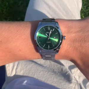 Grön quartzklocka från Doventi  - Snygg klocka från Doventi med grön urtavla och silverfärgat armband i metall. Klockan har datumvisning och stilrena indexmarkeringar. Den har en klassisk rund form och passar perfekt för dig som gillar en modern och fräsch look.