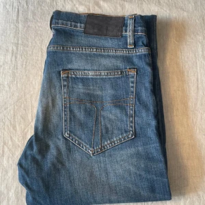Blå jeans från tiger of Sweden - Snygga blå jeans från T/J i modellen Pistolero. Klassisk femficksdesign med kontrastsömmar och läderpatch bak i midjan. Jeansen har en rak passform och är tillverkade i slitstarkt denimtyg. Perfekta för dig som gillar en tidlös look.