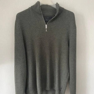 Grön stickad tröja  - Mörkgrön stickad tröja från Jack & Jones med half zip-dragkedja och hög krage. Tröjan har lång ärm och en clean, stilren look som passar perfekt till jeans eller chinos. Skön och mjuk känsla, perfekt för kyligare dagar.