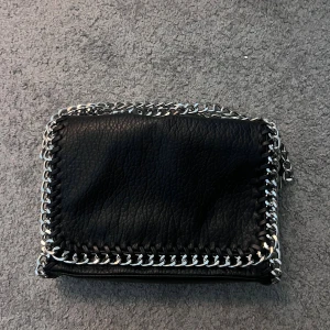 Tiamo väska  - Snygg svart axelväska från Tiamo i skinnimitation med grova silverfärgade kedjor runt kanterna och som axelrem. Väskan har magnetlås, innerfack med dragkedja och är perfekt för att lyfta vilken outfit som helst. 600kr nypris.💕