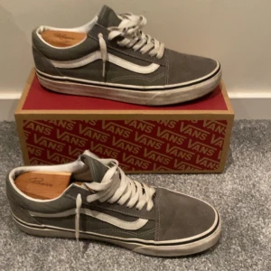 Gråa Vans Old Skool sneakers - Klassiska Vans Old Skool sneakers i grå mocka och canvas med vit sidostripe och vita snören. Skorna har en låg profil, platt sula och rund tå. Perfekta för en avslappnad streetstyle-look.
