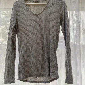 Grå ribbad långärmad tröja - En enkel och stilren grå långärmad tröja med ribbat mönster och v-ringning. Perfekt basplagg som funkar året runt och är lätt att matcha med andra kläder. Mjuk och skön känsla mot huden.