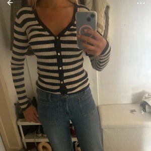 Randig kofta från Filippa K, svart/vit - Supersnygg ribbad kofta från Filippa K i svart och vitt. Den har smala horisontella ränder, v-ringning och knappar framtill. Långärmad och figurnära passform, perfekt att styla med jeans eller kjol. Materialet är mjukt och stretchigt för en bekväm känsla.