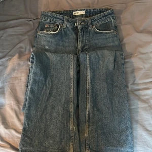 Blå raka jeans från Gina Tricot - Säljer ett par klassiska blå jeans från Gina Tricot med raka ben och normal passform. Jeansen har fem fickor, dragkedja och knapp i midjan. De är rätt höga i midjan. De är slitna i slutet av benen och säljer därför de billigt, annars i jättebra skick 