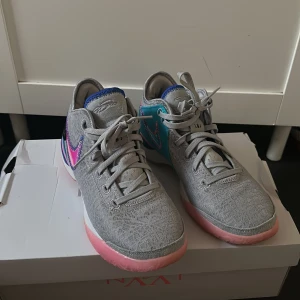 Grå Nike sneakers med färgglada detaljer - Säljer ett par grå Nike sneakers med snygga rosa och blå detaljer. Skorna har ett stickat mönster, rosa sula och coolt broderad Swoosh i lila och rosa. Insidan är blå och baksidan har turkosa och rosa inslag. Perfekta för dig som vill sticka ut.