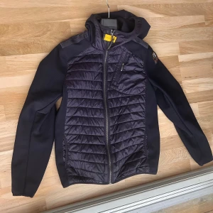 Mörkblå pufferjacka från Parajumpers - Säljer en mörkblå pufferjacka från Parajumpers med huva och hel dragkedja. Jackan har quiltade partier framtill och baktill, samt släta ärmar och sidor. Praktiska fickor med dragkedja och en snygg logga på ärmen. Perfekt för kyliga dagar. Den passar till folk som är mellan 165-175 cm