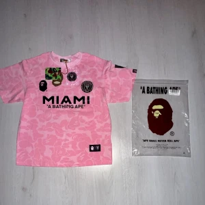 BAPE Miami Jersey Pink – Limited Edition Streetwear - Selling a pink BAPE Miami jersey. The jersey has only been tried on but unfortunately didn’t fit me – so it is in brand new condition.  ✅ Color: Pink ✅ Condition: New – only tried on ✅ Perfect for anyone who loves designer clothing, streetwear, and football jerseys.  A really stylish and unique piece from A Bathing Ape (BAPE) that stands out both for everyday wear and as a streetwear statement.