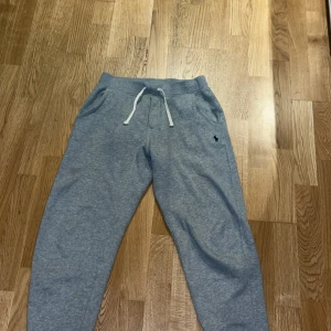 Grå mjukisbyxor Polo Ralph Lauren M - Grå mjukisbyxor från Polo Ralph Lauren med vit snörning i midjan och klassisk logga på ena benet. Byxorna har normal passform, resår i midjan och muddar vid bensluten. Perfekta för chill dagar eller när du vill vara bekväm. Använd 1 gång 
