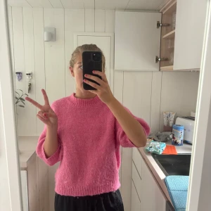 Rosa stickad tröja med kort ärm - Superfin rosa stickad tröja med korta, lite puffiga ärmar och ribbade muddar. Tröjan har en rund halsringning och är perfekt för dig som vill ha en färgklick i garderoben. Mjuk och skön, passar till både jeans och kjol.