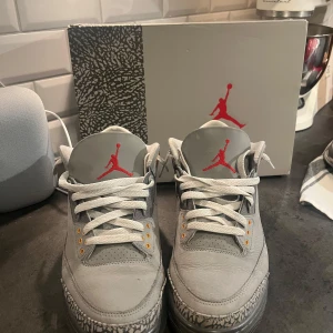 Nike Air Jordan 3 Retro Cool Grey - Nike Air Jordan 3 Retro Cool Grey med grå mocka och läder, vita snören och ikoniska elefantmönster på tån och hälen. Röd Jordan logga på plösen och baksidan, samt gula detaljer vid snörningen. Perfekta sneakers för dig som vill sticka ut🤙🙏