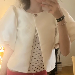 Vit kort kavaj med puffärmar - Superfin vit kavaj med stora puffärmar och rund halsringning. Stängs med en knapp framtill och har en croppad passform. Snygg och trendig modell som ger en cool siluett. Perfekt för dig som vill sticka ut med en unik jacka.