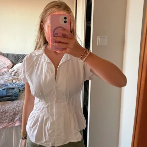 Vit kortärmad skjorta med knappar - Snygg vit skjorta med korta ärmar och klassisk krage. Figursydd modell med knäppning framtill. Perfekt till jeans eller kjol för en clean look. Gjord i mjukt bomullstyg som andas.