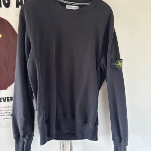 Svart Stone Island sweatshirt L - Svart sweatshirt från Stone Island i 100% bomull med klassisk rund hals och ikonisk patch på vänster ärm. Tröjan har långa ärmar och ribbade muddar. Perfekt för dig som gillar streetwear och vill ha en clean look.