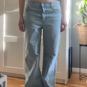 Ljusblå wide jeans från Zara - Säljer ett par ljusblå jeans från Zara i storlek 36. Modellen har raka ben med wide fit och klassiska fem fickor. Jeansen är tillverkade i jeansmaterial med snygga kontrastsömmar och knappstängning framtill. Perfekt för en chill och trendig look. De är lite uppsydda i benen, jag är 170 som referens.