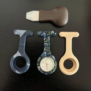 Blommig sjuksköterskeklocka med extra skal - Säljer en blommig sjuksköterskeklocka med analog urtavla och två extra silikonfodral, ett i beige och ett i blått med randigt mönster. Följer även med en boettkniv för enklare batteribyte.