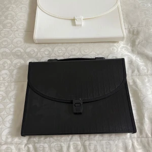 Svart och vit portfölj med fack - Två portföljer i svart och vitt med praktiska handtag och smidig låsning. Insidan har flera fack för att organisera papper eller dokument. Perfekt för skola eller jobb när du vill hålla ordning på allt viktigt. Tillverkade i syntetmaterial med stilren, enkel design.