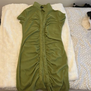 Grön kortklänning från SHEIN - Snygg grön kortklänning från SHEIN med korta ärmar och hög krage. Klänningen har knappar hela vägen framtill och cool rynkdetalj längs knappraden. Tillverkad i mjukt, stretchigt material som känns bekvämt mot huden.