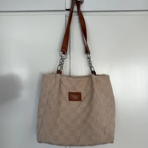 Beige axelväska från Maidudle - Snygg beige axelväska från Maidudle med rutigt mönster i tyg och bruna axelremmar i konstläder med kedjedetaljer. Perfekt storlek för vardagens alla prylar och har en stilren look som passar till det mesta.