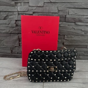 Svart quiltad axelväska Valentino - Säljer en svart quiltad axelväska från Valentino Garavani med ikoniska guldfärgade nitar och kedjerem. Väskan är i skinn och har ett snyggt lås framtill. Perfekt för dig som vill ha en edgy och lyxig accessoar med statement-detaljer. Går ner i pris enbart vid möte i göteborg❤️