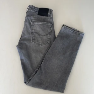 Grå Jack & Jones Jeans - Snygga grå jeans från Jack & Jones i modellen Tapered/Mike. Jeansen har klassisk femficksdesign, dragkedjegylf och coolt tvättad look. Passformen är tapered vilket ger en modern siluett. Perfekta till sneakers och hoodie. Nypris 900kr, mitt pris 399kr