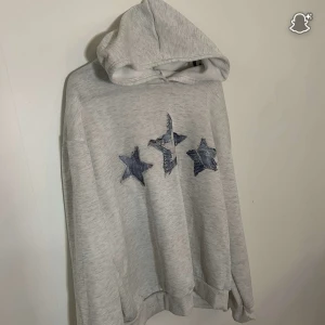 Grå mjukissätt med stjärnor från Shein - Grå mjukisshorts från Shein i storlek XL, med elastisk midja och tre blå stjärnor broderade på ena benet. Sköna och avslappnade shorts i mjukt material, perfekta för chill dagar eller träning. Hoodie i storlek XL från Shein. 