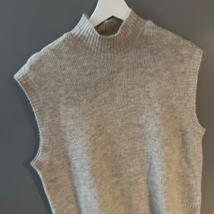 Beige stickad väst  - beige stickad väst från Vero Moda med ribbad struktur och hög krage. 