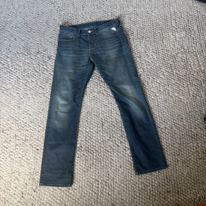 Blå Replay jeans straight fit - Säljer ett par blå jeans från Replay med klassisk femficksdesign och snygga slitningar. Jeansen har rak passform och normal midja, med Replay-logga i metall på fickan. Perfekta för dig som gillar en tidlös och avslappnad stil.
