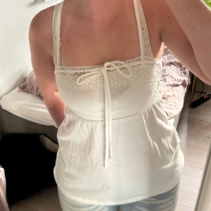 Vit topp med spetsdetaljer från Hollister - Supersöt vit topp från Hollister med smala axelband, spetsdetaljer upptill och knytband framtill. I nyskick fast utan prislapp, aldrig använd och köpt på Hollister i Nice❤️Storlek XS men passar också S. Använd gärna köp nu❣️