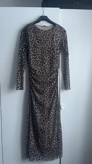 Leopardmönstrad långklänning Kappahl - Säljer en långärmad långklänning från Kappahl i storlek S med leopardmönster. Klänningen har en figurnära passform och är gjord i ett stretchigt syntetmaterial. Färgerna går i beige och brunt med svarta detaljer. Perfekt för dig som vill sticka ut lite extra.