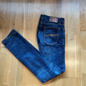 Mörkblå skinny/slim jeans från Nudie Jeans - Säljer ett par mörkblå slim jeans från Nudie Jeans med snygga detaljer på bakfickorna. Jeansen har normal passform i midjan och är tillverkade i stretchig bomullsdenim. Perfekt för dig som gillar en stilren look. Storlek(w28 L32) (“nästan nyskick”, “knappt använda“nypris ca 1 600 kr”)  kan gå ner i pris vid snabb affär