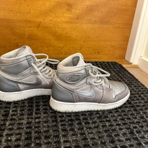 Nike Air Jordan 1 Silver sneakers - Säljer ett par Nike Air Jordan 1 i metallic silver. Klassisk high-top modell med snörning, rund tå och vit sula. Skorna är i skinn och har ikoniska Jordan Wings-loggan på sidan. Perfekta för dig som vill sticka ut med en clean och modern look.