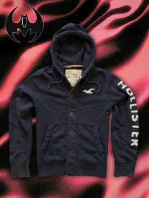 Mörkblå Hollister Kofta (Sällsynt) - Mörkblå kofta med tryck | extremt sällsynt | pris kan diskuteras | Mycket bra skick | size M/L | längd: 67 cm Axelbredd: 46cm Armlängd: 72cm (Passform & Längd kan variera)