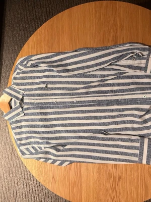 Randig skjorta från Lacoste, blå/vit - Säljer en fräsch skjorta från Lacoste i storlek S med blå och vita horisontella ränder. Skjortan har klassisk krage, knappar hela vägen och den ikoniska krokodilloggan på bröstet. Materialet är mjuk bomull, perfekt för dig som gillar stilren design. Tyvärr är skjortan inte autentisk men kvaliteten är väldigt bra , hör av dig vid minsta fundering eller lägg ett prisförslag 😇
