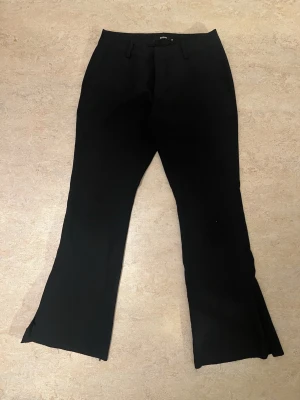 Svarta vera kostymbyxor - Snygga svarta kostymbyxor med bootcut passform och pressveck. Byxorna har fickor fram, bälteshällor och diskreta slitsar vid bensluten. Perfekta för en clean och stilren look.