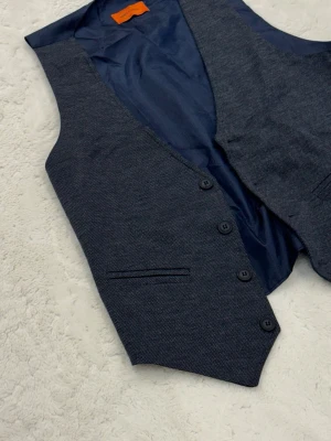 Mörkblå kostymväst med knappar - Snygg mörkblå kostymväst från Selected Homme med fyra knappar framtill och diskreta fickor. Västen har en klassisk v-ringad form och är fodrad på insidan för extra komfort. Perfekt att styla över skjorta för en clean look.