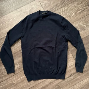 Mörkblå tröja från MNG MAN - En stilren mörkblå tröja från MNG MAN i klassisk modell med rund halsringning och långa ärmar. Tröjan är tillverkad i mjuk bomull och har ribbade muddar vid ärmslut och nederkant. Perfekt för lager-på-lager under hösten och vintern. Den är lite urtvättad därav priset